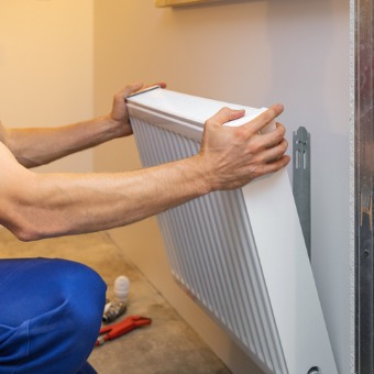 A heating technician placing a heating unit on the wall during heating repair in Bloomington IL