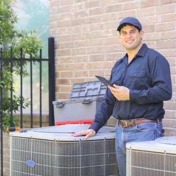 A repairman smiles by a A/C and heating unit. Chambers Services offers more than Refrigerator Repair in Bloomington IL.
