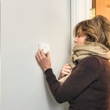 A cold woman adjusts her heat before calling for Furnace Repair in Bloomington IL