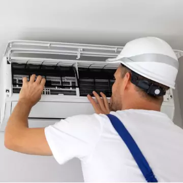 A technician checking the inside of a wall-mounted AC unit as part of his AC Repair process