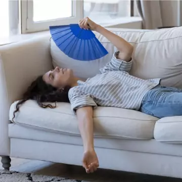 An exhausted young woman fanning herself due to the excessive heat and humidity in her home, needing a dehumidifier from Chambers Services