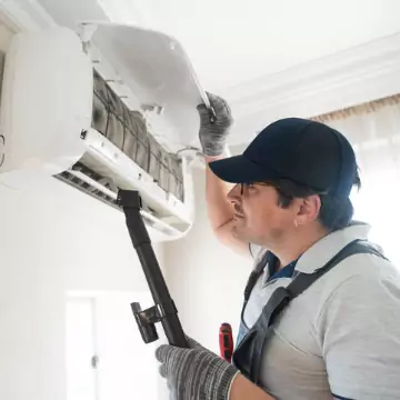 An AC tech cleaning out a wall-mounted AC unit as part of AC maintenance in Central Illinois