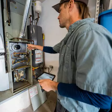 A young man performing furnace repair on a unit in a Peoria, IL home