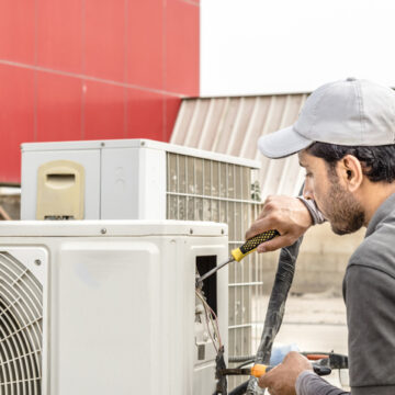 Air Conditioning Contractor Bloomington IL, a professional an electrician repairman is repairing a heavy duty central air conditioner unite at the roof top and wearing blue uniform