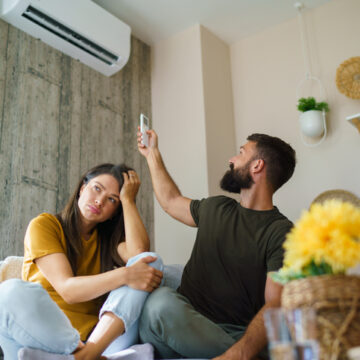 Air Conditioning Repair Bloomington IL, Frustrated couple trying to turn on a broken air conditioner inside their hot living room